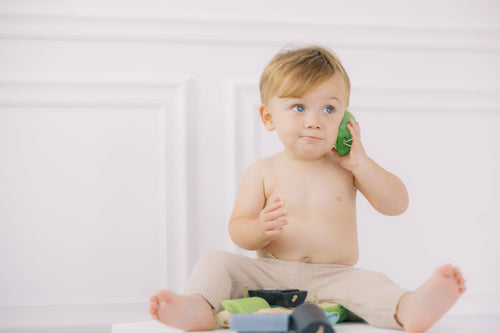 Baby holding a green Envy U cleanser bar to his ear like a phone